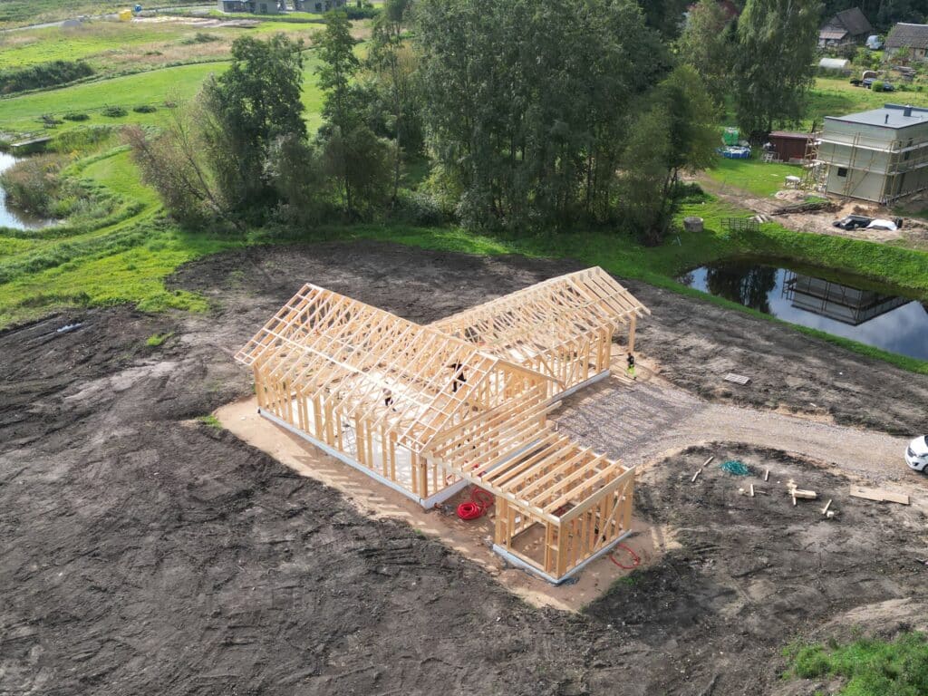 Skats no augšas uz koka karkasa māju ar uzstādītām jumta kopnēm un piebūvēm.